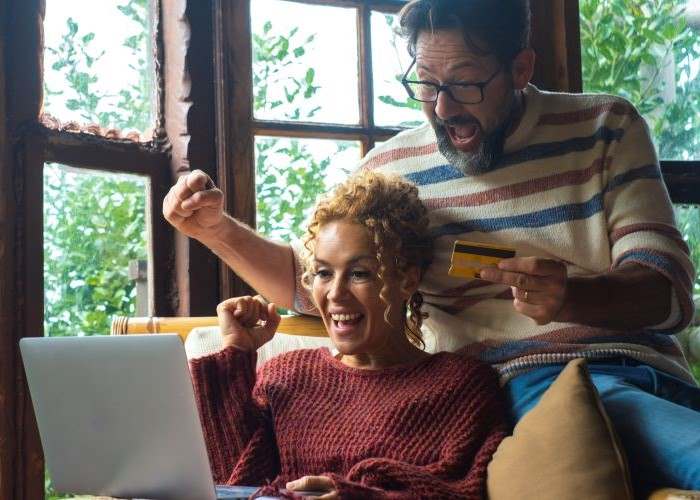 Couple sitting on couch in joyful mood looking at laptop